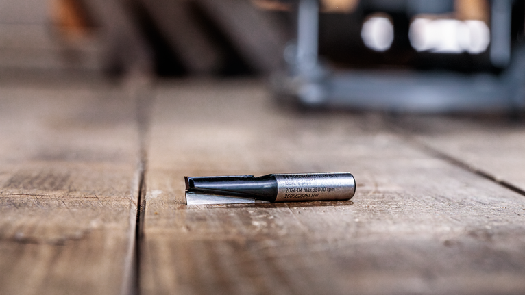 PRO Router Straight Bit, Two Flutes, Ø 1/4″ x L 5/8″, Shank 1/4″ Router bit lying on a wooden surface in a workshop setting.