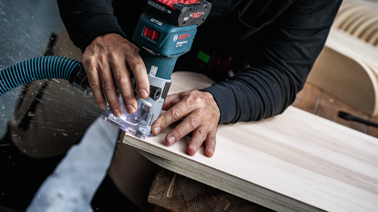 Person smooths edge of a wooden board using a cordless router.
