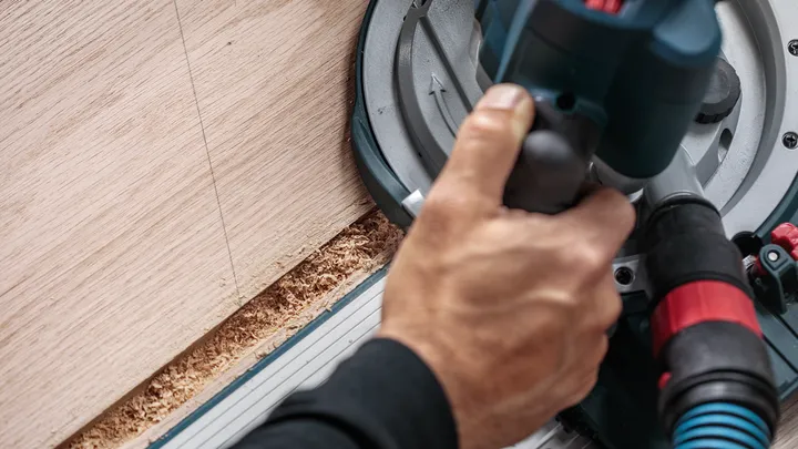 Person operates a circular saw to cut wood along a straight line.
