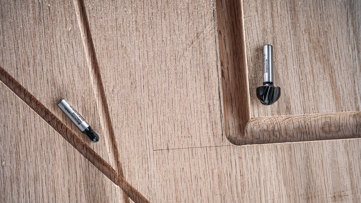 Two router bits rest on a carved wooden surface with grooved details.