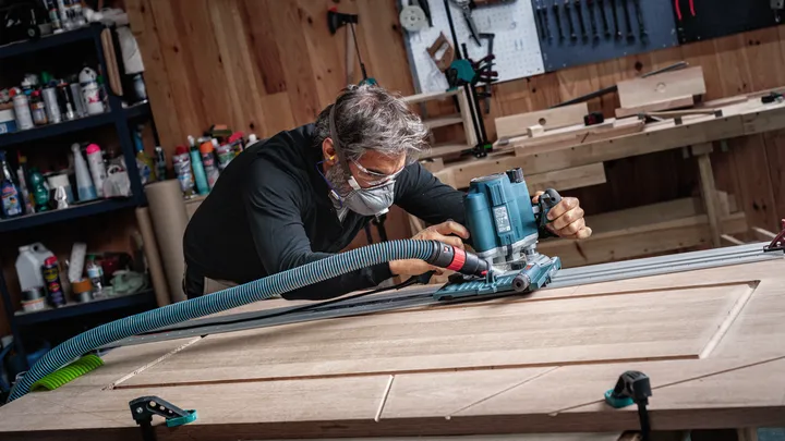 Person wearing safety equipment uses a power tool to rout grooves in a wooden door.