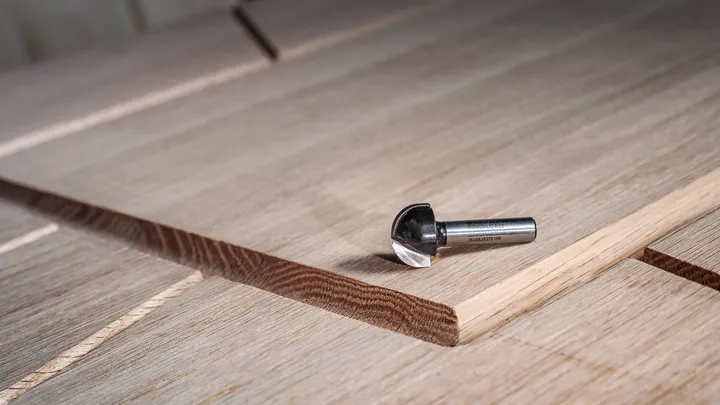 Carbide router bit resting on layered wood panel with a freshly cut groove.