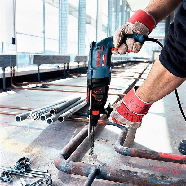 A person wearing safety equipment drills into a metal pipe at a construction site.