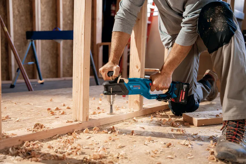 A person wearing safety equipment drills a wooden frame with a cordless angle drill.
