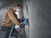Person wearing safety equipment uses a power tool to cut a straight line on a concrete wall.