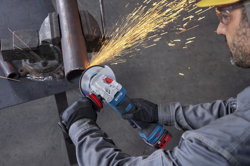 GWS18V-11PS A person wearing safety equipment grinds a metal pipe with an angle grinder, creating sparks.