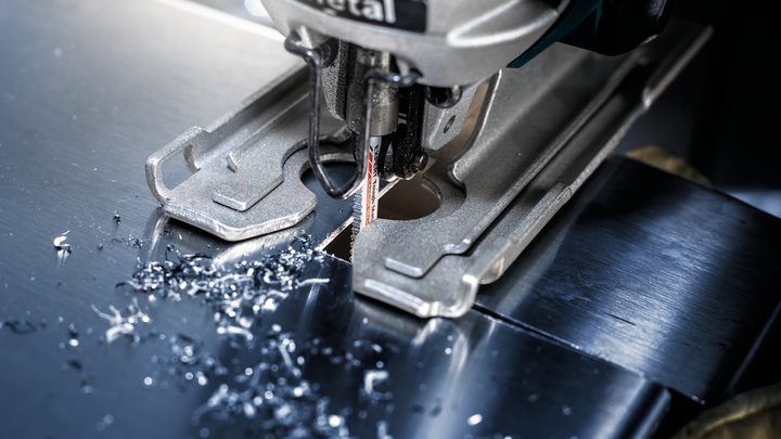 Jigsaw cutting a precise hole through a shiny metal sheet.