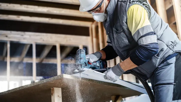 Object #200597854: 2793289_app_web_05 Person wearing safety equipment cuts a board with a power tool in a construction area.