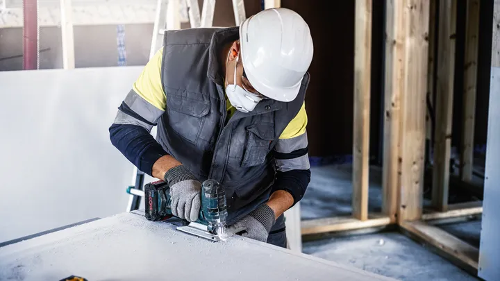 Object #200597855: 2793289_app_web_04 A person wearing safety equipment cuts drywall with a jigsaw.