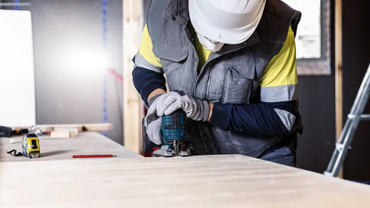 Object #200597865: 2793296_app_web_06 Person wearing safety equipment uses a power tool to cut wood at a workbench.