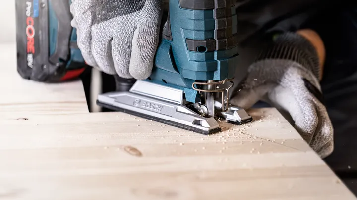 Object #200597866: 2793296_app_web_03 Person wearing safety equipment uses a cordless jigsaw to cut a wooden board.