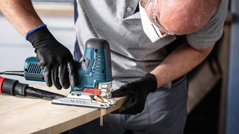 EXPERT Wood 2-side clean T308BO Jigsaw Blade, 5 pcs Person wearing safety equipment cuts wood using a power jigsaw.