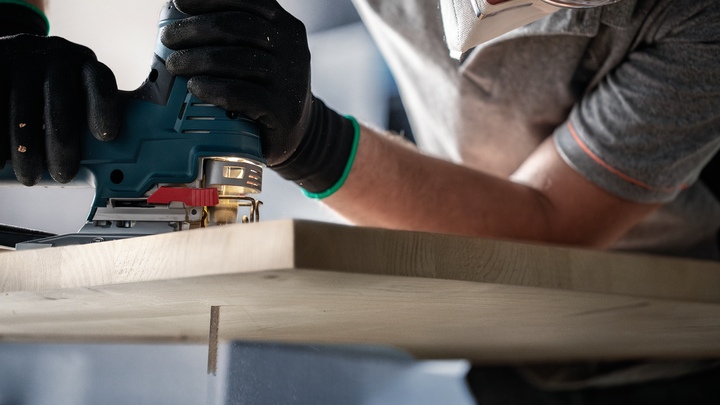 Object #200597873: 2793297_app_web_04 Person wearing safety equipment uses a jigsaw to cut a wooden board.