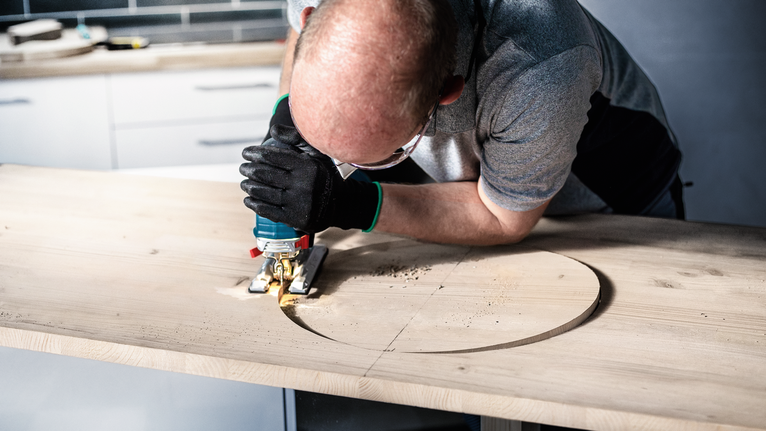 EXPERT Wood 2-side clean T308BO Jigsaw Blade, 5 pcs Person wearing safety equipment uses a jigsaw to cut a circle in a wooden board.