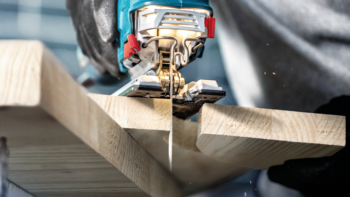 Object #200597875: 2793297_app_web_05 Person guides a jigsaw to cut a wooden plank, wearing safety equipment.