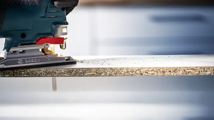 Object #200597890: 2793295_app_web_06 Person wearing safety equipment uses a jigsaw to cut a laminated board.