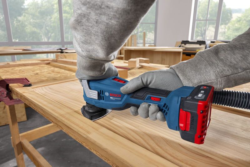 A person wearing safety equipment sands a wooden board with a multifunction tool.