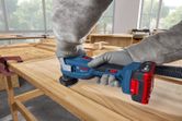 A person wearing safety equipment sands a wooden board with a multifunction tool.