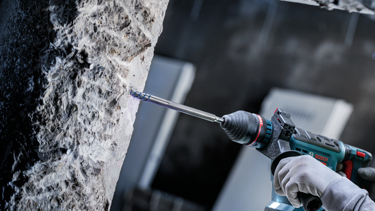 Person wearing safety equipment drills into concrete using a power tool.