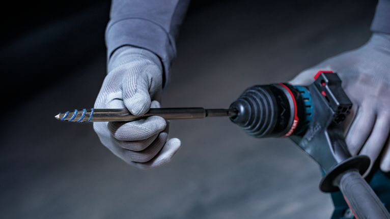 Person wearing safety equipment inserts a drill bit into a power tool.