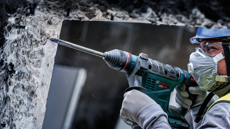 A person wearing safety equipment drills into a concrete wall.