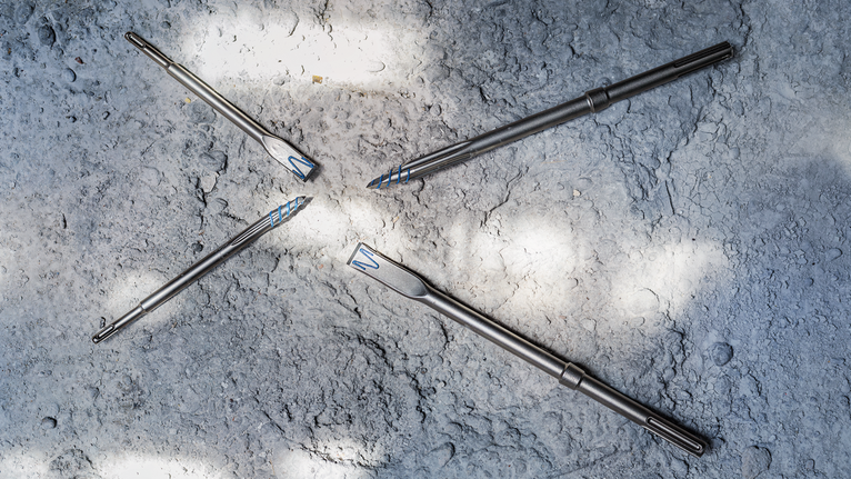 Four metal drill bits arranged on a rough concrete surface.
