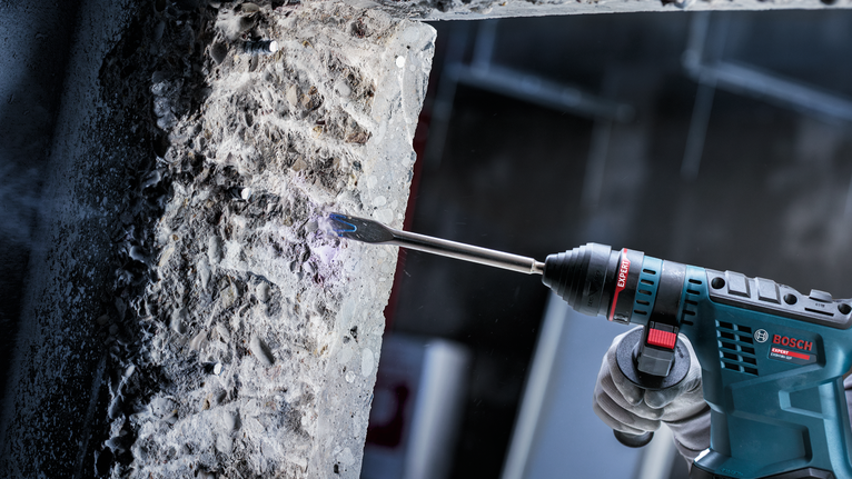 Person wearing safety equipment uses a rotary hammer to chip away at concrete.