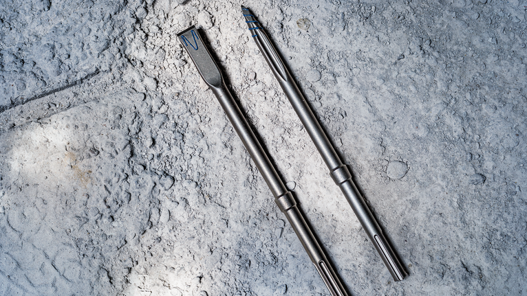 Two metal drill bits lie on rough concrete.