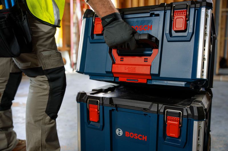 A person wearing safety equipment lifts a blue carrying case system with a black handle.