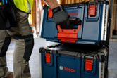 A person wearing safety equipment lifts a blue carrying case system with a black handle.