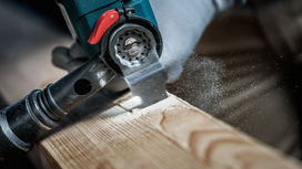 Person wearing safety equipment cuts wood with a power tool, sawdust spraying.