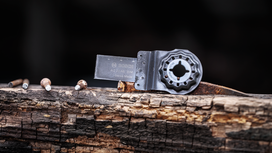 Oscillating multi-tool blade resting on a weathered wooden beam beside four nails.