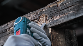 Person wearing safety equipment uses a power tool to extract a nail from damaged wood.