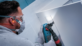 Person wearing safety equipment cuts through a panel with a power tool.