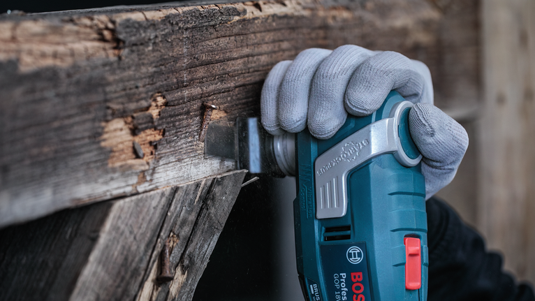 Person wearing safety equipment uses a power tool to cut into a wooden beam.
