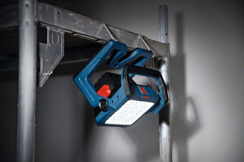 Cordless jobsite light mounted on metal scaffolding, illuminating a dim workspace.