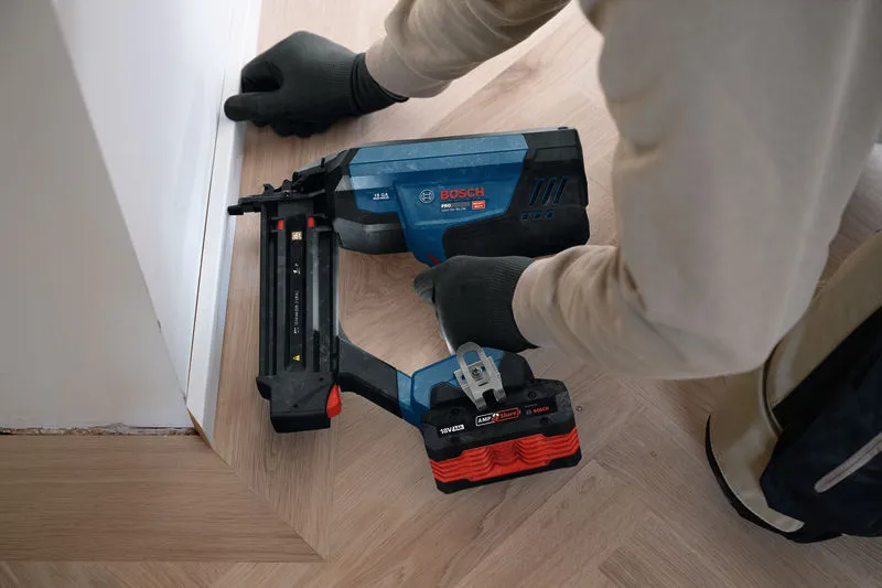 Person wearing safety equipment uses a cordless brad nailer to install floor trim.