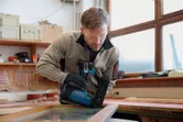 A person wearing safety equipment uses a cordless brad nailer to fasten wood.