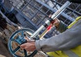 A person wearing safety equipment measures distance with a large measuring wheel.