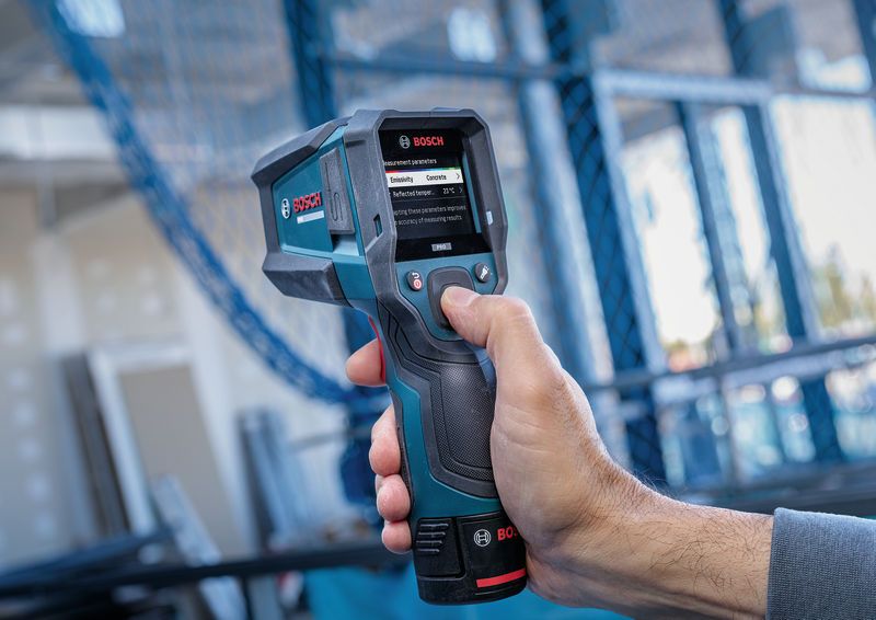 Person operating a thermo detector with a digital display at a construction site.