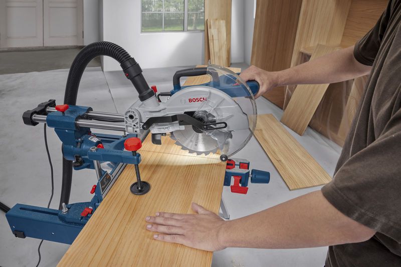 A person operates a mitre saw to cut a wood board in a workshop.