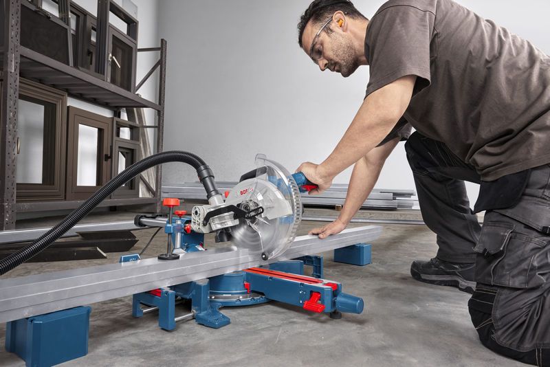 A person wearing safety equipment cuts a metal beam using a mitre saw.