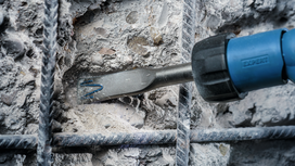 Chisel tool breaking concrete between metal reinforcement bars.