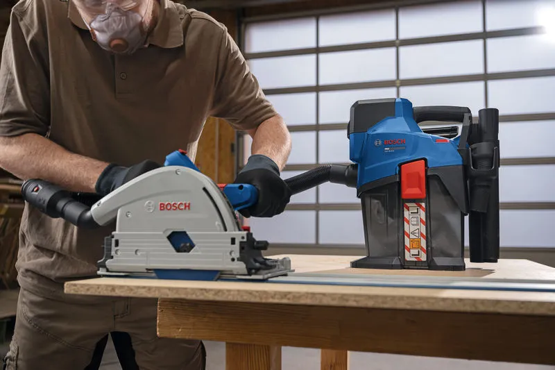 A person wearing safety equipment operates a dust extractor while cutting wood.