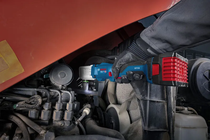 A person wearing safety equipment uses a cordless impact wrench on an engine.
