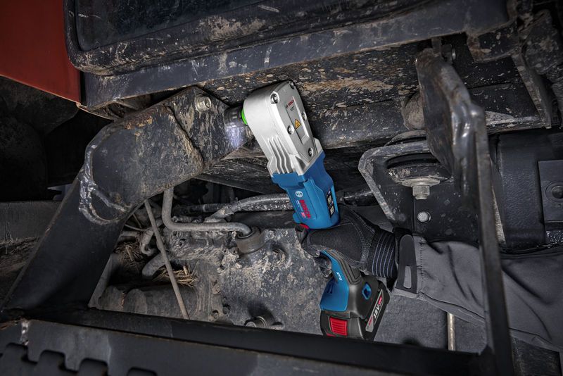 A person wearing safety equipment uses a cordless impact wrench on heavy machinery.