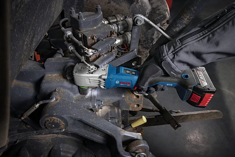 A person wearing safety equipment uses a cordless impact wrench on machinery.