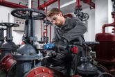 A person wearing safety equipment uses a cordless impact wrench to tighten a valve in an industrial setting.