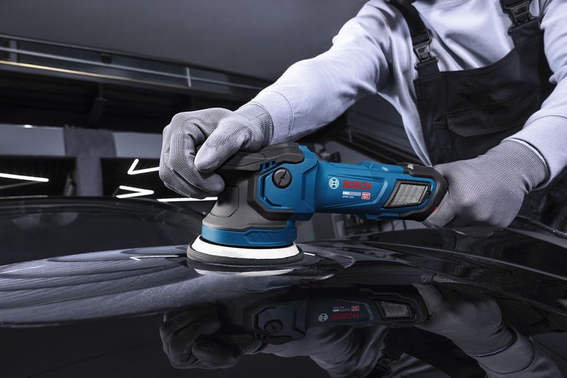 A person wearing safety equipment polishes a car surface with a cordless polisher.