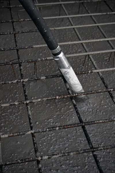 Concrete vibrator consolidating freshly poured concrete over a steel reinforcement grid.